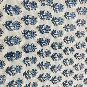 May include: White fabric with a repeating pattern of blue floral designs. The flowers are stylized and have a simple, elegant look.