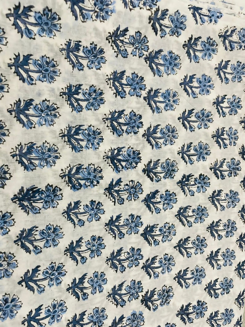 May include: White fabric with a repeating pattern of blue floral designs. The flowers are stylized and have a simple, elegant look.