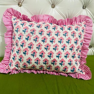 May include: A rectangular throw pillow featuring a repeating floral pattern with pink petals and teal stems on an off-white background. The pillow is framed by a wide, ruffled border with a vibrant pink and white vertical stripe design.