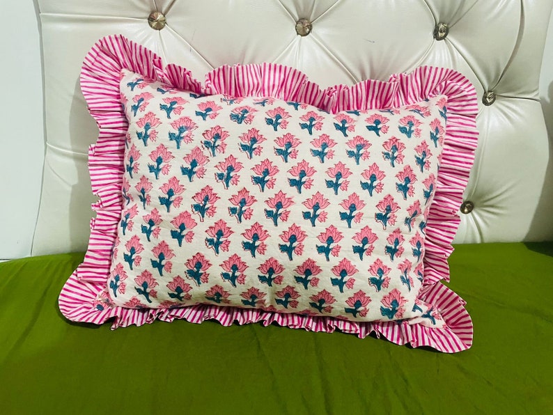 May include: A rectangular throw pillow featuring a repeating floral pattern with pink petals and teal stems on an off-white background. The pillow is framed by a wide, ruffled border with a vibrant pink and white vertical stripe design.