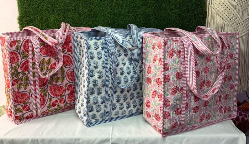 May include: Three tote bags with floral patterns. The bags are made of fabric and have a pink, blue, and white color scheme. The bags have a single strap and are lined with a contrasting color.