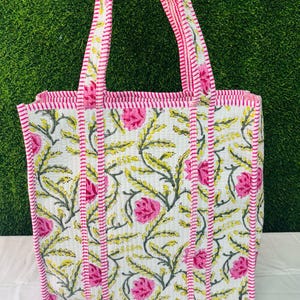 May include: A white tote bag with pink and green floral print. The bag has pink and white striped handles and a pink and white striped trim.