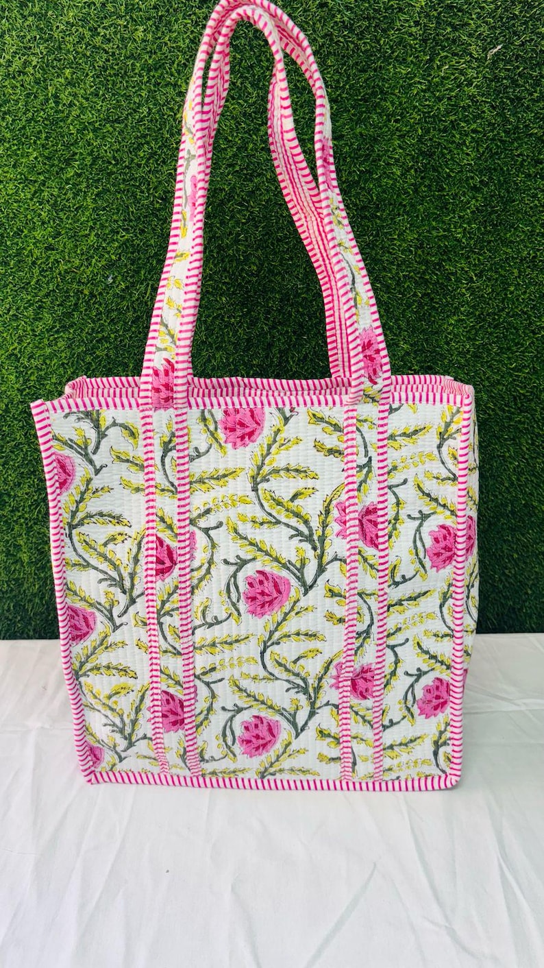 May include: A white tote bag with pink and green floral print. The bag has pink and white striped handles and a pink and white striped trim.