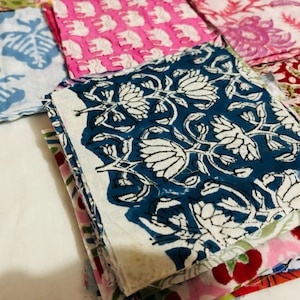 Puede incluir: Una pila de cuadrados de tela coloridos con patrones florales y geom&eacute;tricos. El cuadrado superior es azul con dise&ntilde;os florales blancos. Los otros cuadrados son rosas, rojos y verdes.