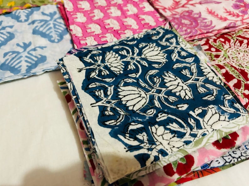 Puede incluir: Una pila de cuadrados de tela coloridos con patrones florales y geom&eacute;tricos. El cuadrado superior es azul con dise&ntilde;os florales blancos. Los otros cuadrados son rosas, rojos y verdes.