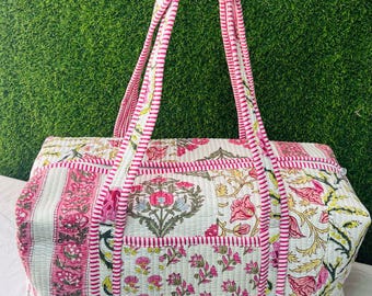 May include: A quilted tote bag with a floral pattern in pink, white, and green. The bag has two handles and a rectangular shape. The bag's dimensions are approximately 18 inches long, 10 inches high, and 8 inches wide.