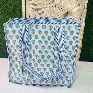 May include: A white tote bag with blue floral print and blue and white striped handles. The bag is made of cotton and has a quilted design.