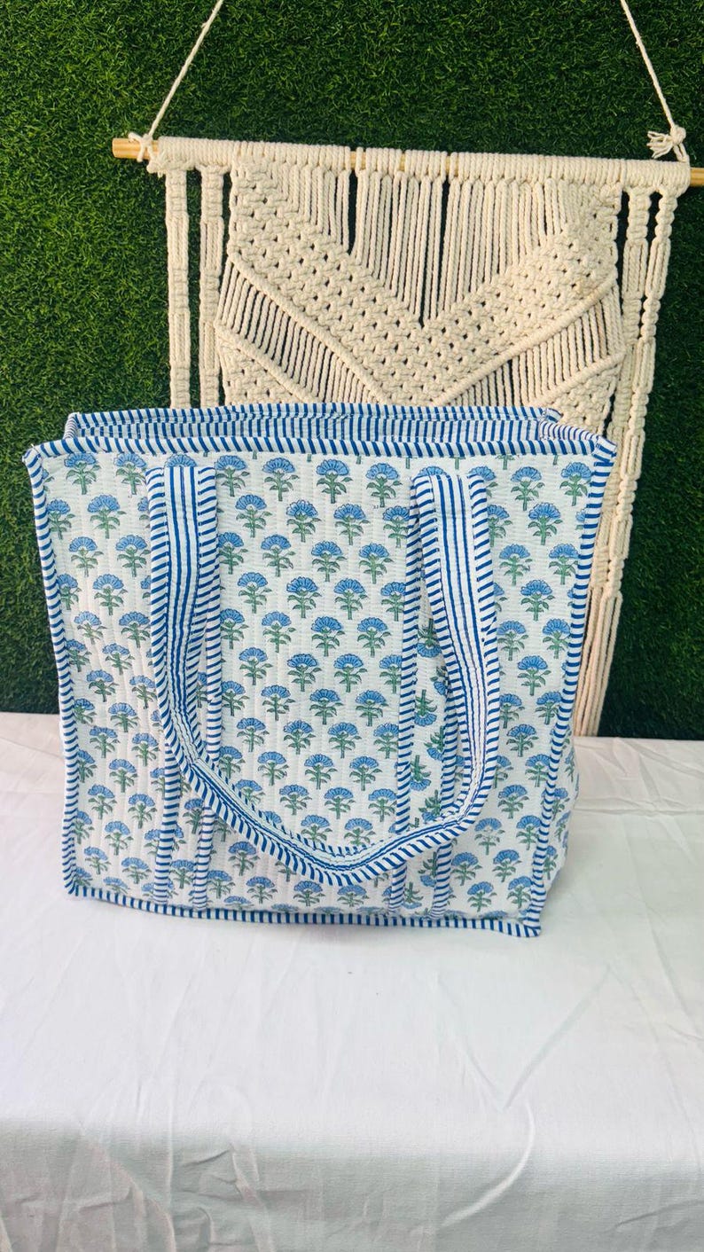 May include: A white tote bag with blue floral print and blue and white striped handles. The bag is made of cotton and has a quilted design.