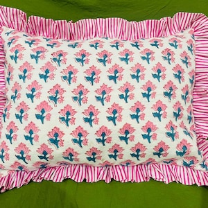 May include: A rectangular pillow featuring a white base with a repeating pattern of pink flowers and blue stems. The pillow is bordered by a wide, gathered ruffle trim in a pink and white vertical stripe pattern, creating a decorative edge.