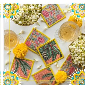 May include: Set of six colorful fabric coasters with floral and leaf patterns. The coasters have a yellow border and are arranged on a white surface with flowers and a glass of wine.