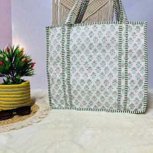 Pu&ograve; includere: Una borsa tote bianca con strisce verdi e bianche e un motivo floreale. La borsa ha due manici lunghi.