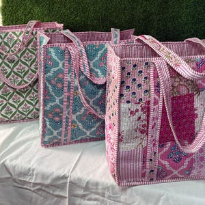 May include: Three quilted tote bags with floral patterns. The bags are pink, green, and blue with white accents. The bags have long handles and are made of a soft, quilted fabric.