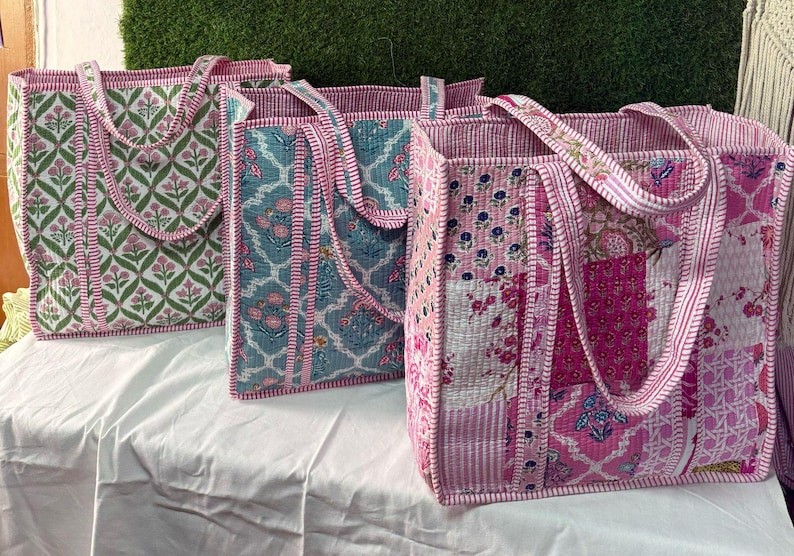 May include: Three quilted tote bags with floral patterns. The bags are pink, green, and blue with white accents. The bags have long handles and are made of a soft, quilted fabric.