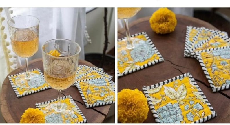 May include: Set of six yellow and blue floral coasters with black and white trim. The coasters are made of fabric and have a quilted design. Two glasses of wine are sitting on the coasters.