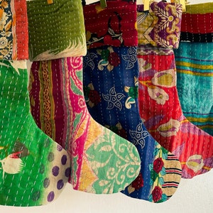 Op de afbeelding: Vijf kleurrijke kerstsokken gemaakt van kantha-stof. De sokken zijn versierd met bloemenpatronen en hebben een patchwork-ontwerp.
