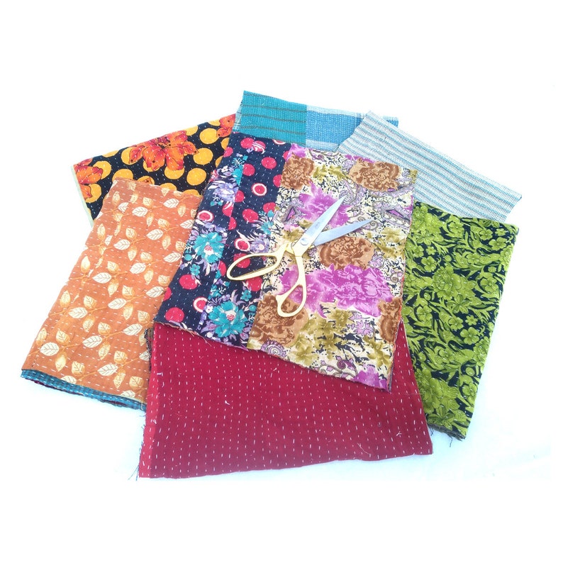 May include: A collection of colorful fabric scraps with a pair of silver scissors on top. The fabrics are a mix of floral patterns, geometric designs, and solid colors.