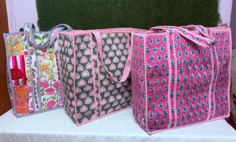 May include: Three tote bags made of quilted fabric with different floral patterns. The bags are pink, green, and blue with white accents. The bags have two handles and are made of a soft, durable fabric.