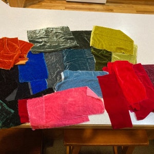 May include: A selection of velvet fabric swatches in shades of red, pink, blue, green, and gold. The fabric pieces are displayed on a white surface, highlighting their textures and colours. Measurements are not available.