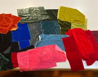 Könnte beinhalten: Eine Sammlung farbenfroher Samtstoffmuster in verschiedenen Rot-, Rosa-, Blau-, Grün- und Goldtönen. Die Stoffstücke sind auf einer weißen Oberfläche angeordnet und zeigen ihre Texturen und Farben.