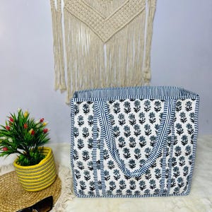 May include: A white tote bag with blue and black floral print. The bag has two blue and white striped handles.