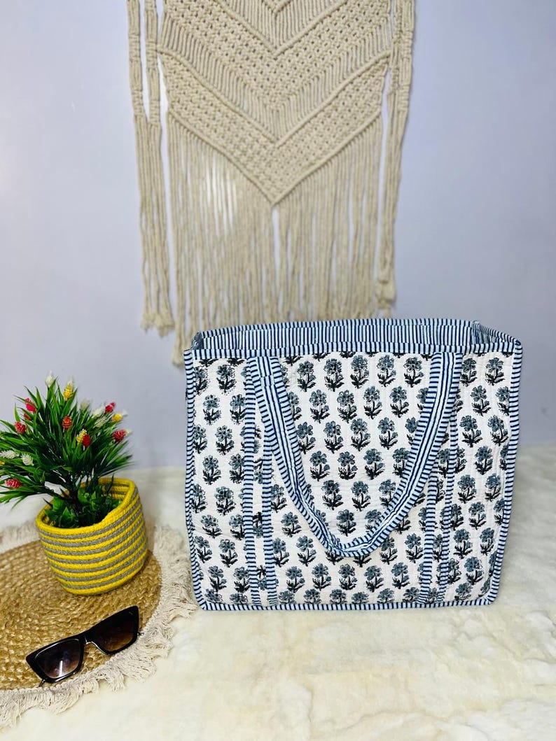 May include: A white tote bag with blue and black floral print. The bag has two blue and white striped handles.