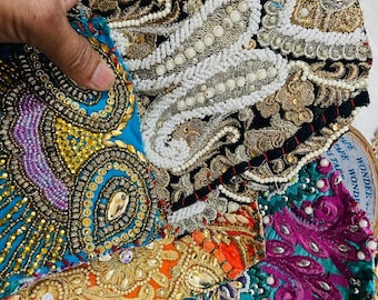 May include: A collection of colorful fabric scraps with intricate embroidery and beading. The fabrics are in shades of turquoise, black, orange, pink, and green. The embroidery features floral and paisley patterns. The beads are white and gold.
