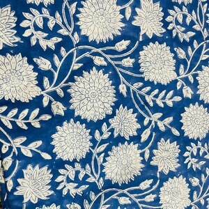 May include: A blue fabric with a white floral pattern. The flowers are stylized and have a circular shape with multiple layers of petals. The fabric has a vintage look and feel.