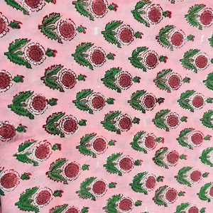 May include: Pink fabric with a repeating pattern of green leaves and red and white flowers.