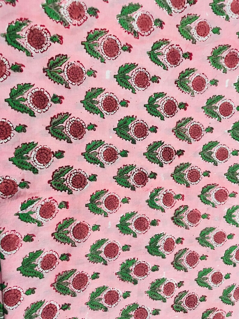 May include: Pink fabric with a repeating pattern of green leaves and red and white flowers.