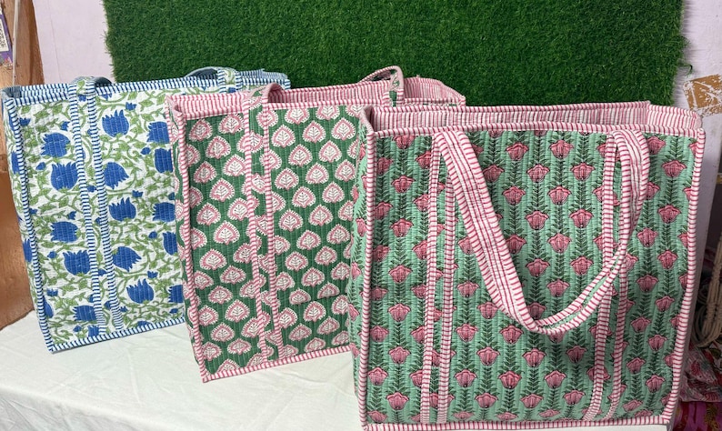 May include: Three tote bags with floral patterns. The bags are made of cotton and have a green, pink, and blue color scheme. The bags have a simple design and are perfect for carrying groceries or other items.