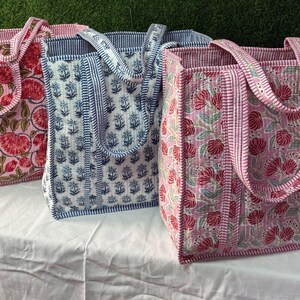 May include: Three tote bags with floral patterns. The bags are made of quilted fabric and have a pink, blue, and white color scheme. The bags have two handles each.