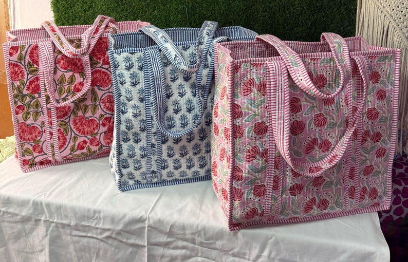 May include: Three tote bags with floral patterns. The bags are made of quilted fabric and have a pink, blue, and white color scheme. The bags have two handles each.