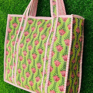May include: A green and pink floral tote bag with white stripes on the handles. The bag is made of quilted fabric and has a floral print.