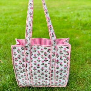 Pu&ograve; includere: Una borsa tote bianca con stampa floreale rosa e verde. La borsa ha manici a righe rosa e bianche.