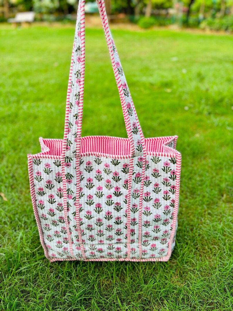 Pu&ograve; includere: Una borsa tote bianca con stampa floreale rosa e verde. La borsa ha manici a righe rosa e bianche.