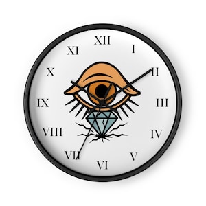 May include: A round wall clock with a black frame and a white face featuring black Roman numerals. The central graphic displays a stylised orange eye with long eyelashes positioned above a light blue diamond shape with black jagged lines.