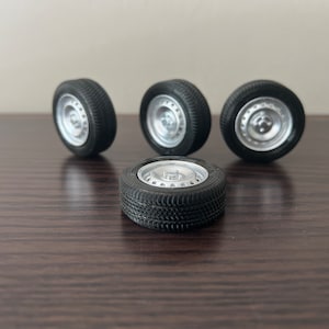 Puede incluir: Cuatro neumáticos de caucho negro con llantas plateadas. Los neumáticos tienen un dibujo de la banda de rodadura y están dispuestos en semicírculo sobre una superficie de madera oscura.