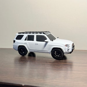 May include: White toy car model of a Toyota 4Runner with a black roof rack and black wheels.