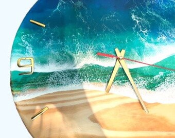 Puede incluir: Un reloj redondo de madera con un diseño de ola de océano de resina azul y verde. La esfera del reloj tiene números y manecillas dorados.