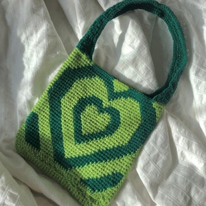 May include: A green and dark green crocheted tote bag with a swirling pattern. The bag has a single strap.