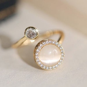 May include: A gold ring with a white stone set in a circle of smaller stones. The ring has a smaller stone on the side.