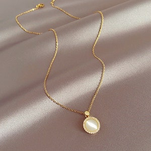May include: A gold chain necklace with a round pendant featuring a white stone surrounded by smaller stones.
