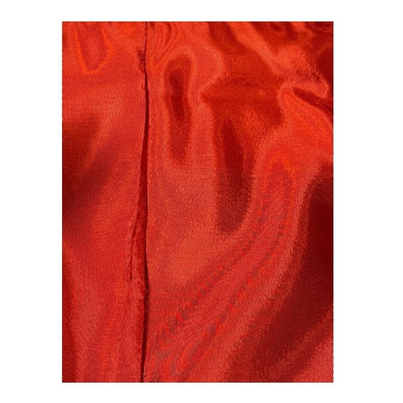 May include: Close-up of a vibrant, solid-colored fabric in a rich shade of red-orange. The material has a subtle sheen, with visible vertical seams running down the center. The texture appears smooth and flowing, suggesting a lightweight textile.