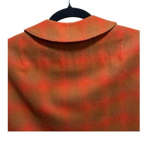 May include: Close-up of a vintage jacket collar and shoulder area. The fabric has a plaid pattern in shades of orange and brown. The jacket is hanging on a black hanger.