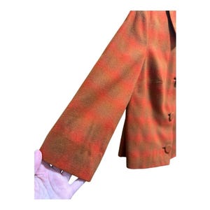 May include: A vintage blazer in a plaid pattern of orange and brown. The blazer has long sleeves and a classic button closure. The fabric appears to be a wool blend, offering a warm and textured look. The blazer is a stylish piece for a retro-inspired wardrobe.