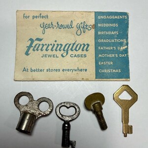 May include: An assortment of vintage keys and a Farrington Jewel Cases advertisement. The keys are in various shapes and colors, including silver, black, and gold. The advertisement is light blue and tan, with text that reads "year-round gifts."