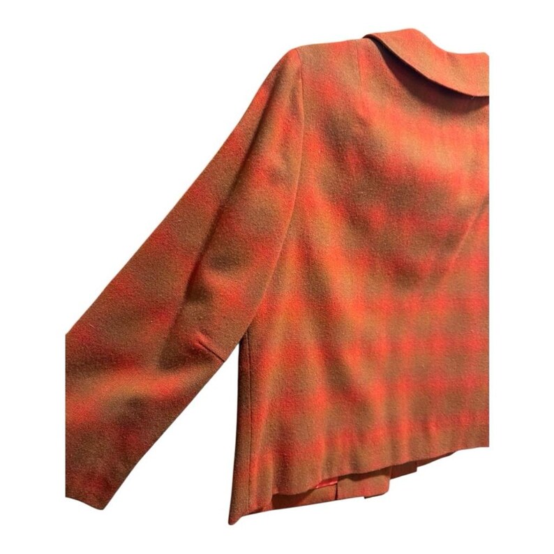 May include: A vintage orange and brown plaid blazer with a classic collar and long sleeves. The jacket features a tailored fit and a two-button closure. The fabric has a textured appearance, suggesting a wool or wool-blend material. The overall style is reminiscent of mid-century fashion.