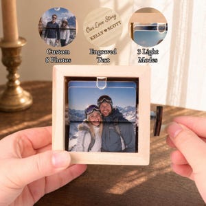 Peut inclure: Un cadre carré en bois clair contenant un présentoir rotatif pour huit photos personnalisées. Le cadre dispose d'une manivelle latérale et d'une source lumineuse interne. La surface en bois porte la gravure Our Love Story KELLY SCOTT.