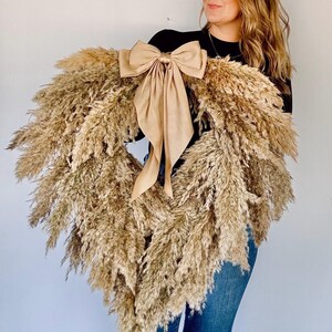 May include: A large heart-shaped wreath made of dried pampas grass with a large beige satin bow.