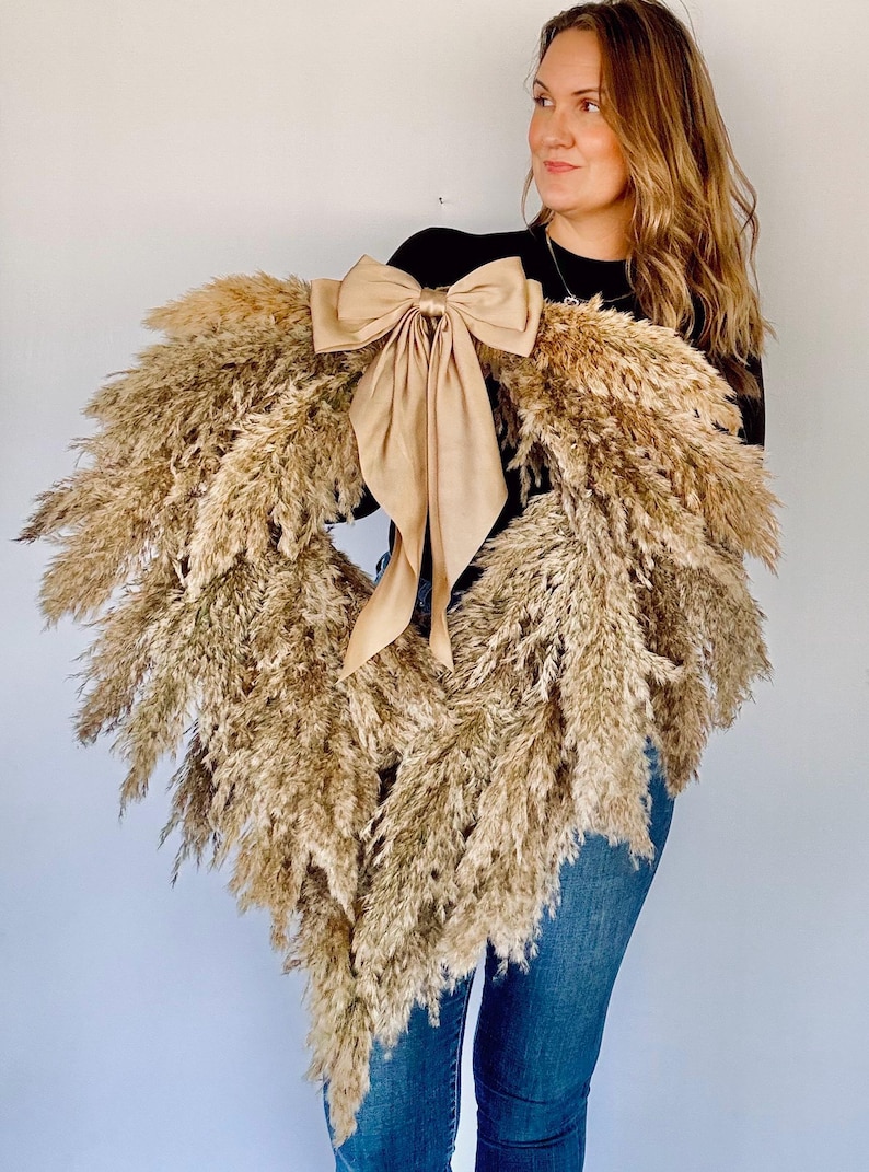 May include: A large heart-shaped wreath made of dried pampas grass with a large beige satin bow.